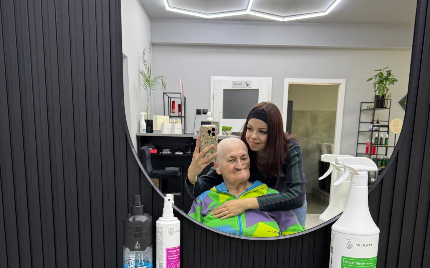 
        Młoda kobieta robi selfie z seniorem w salonie fryzjerskim.
    