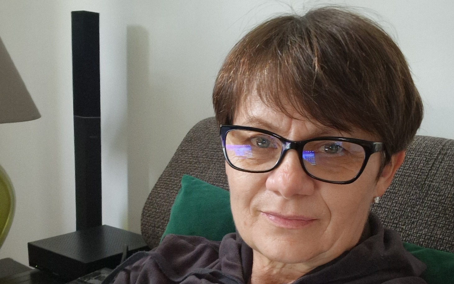 Kobieta w okularach siedzi na kanapie, uśmiechając się.