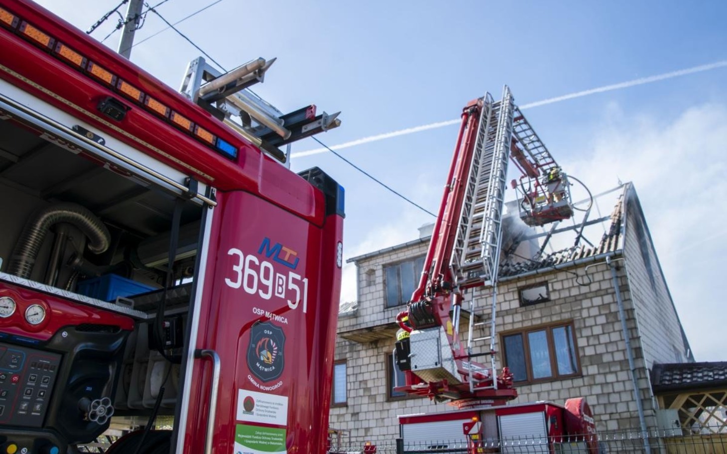
        Strażacy gaszą pożar budynku przy użyciu drabiny i wozu strażackiego.
    