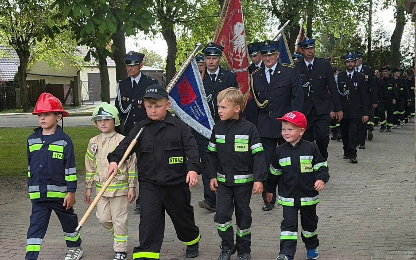 
        Dzieci w mundurach strażackich idą w paradzie.
    