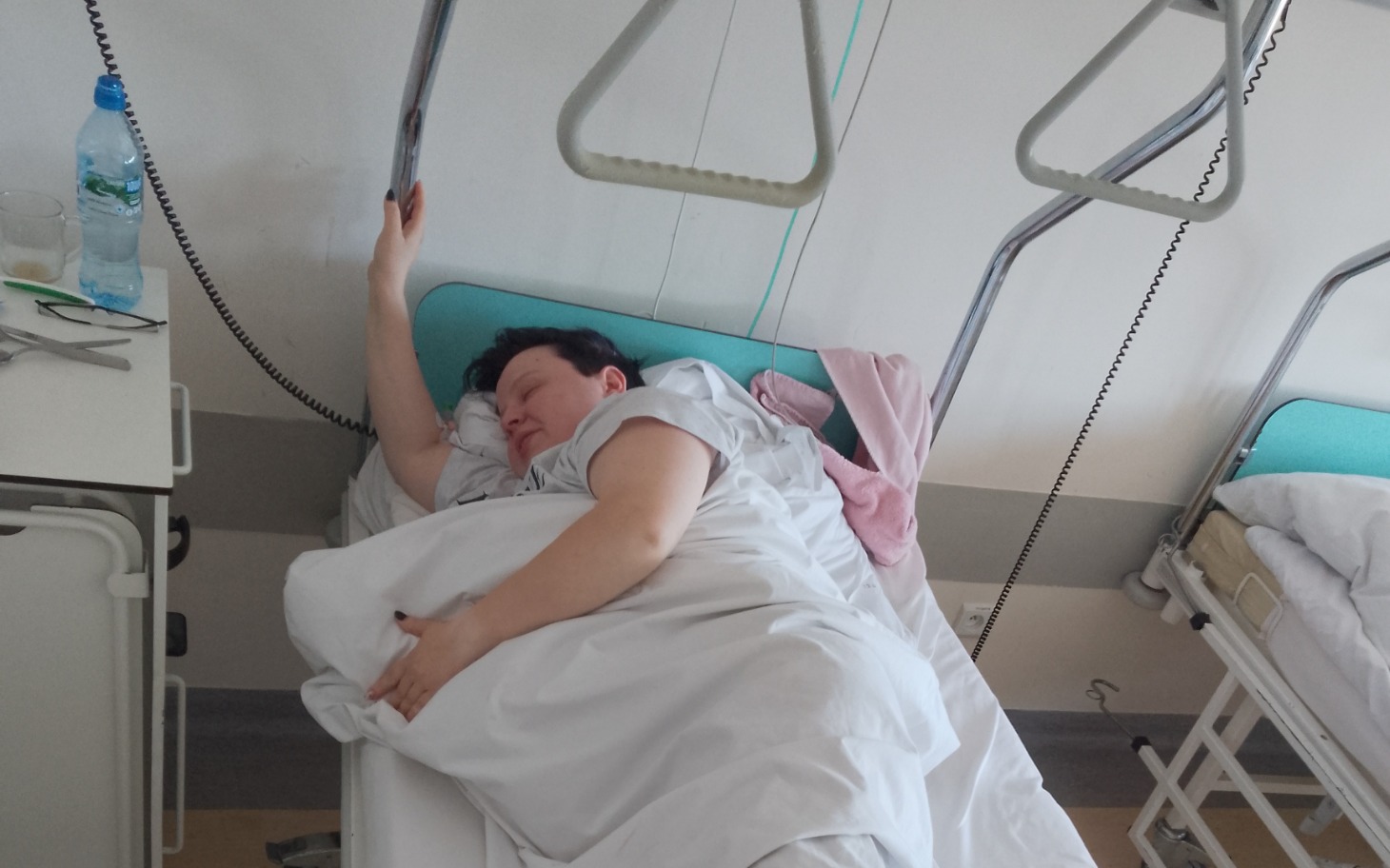 
        Kobieta leżąca w szpitalnym łóżku, przykryta kołdrą.
    