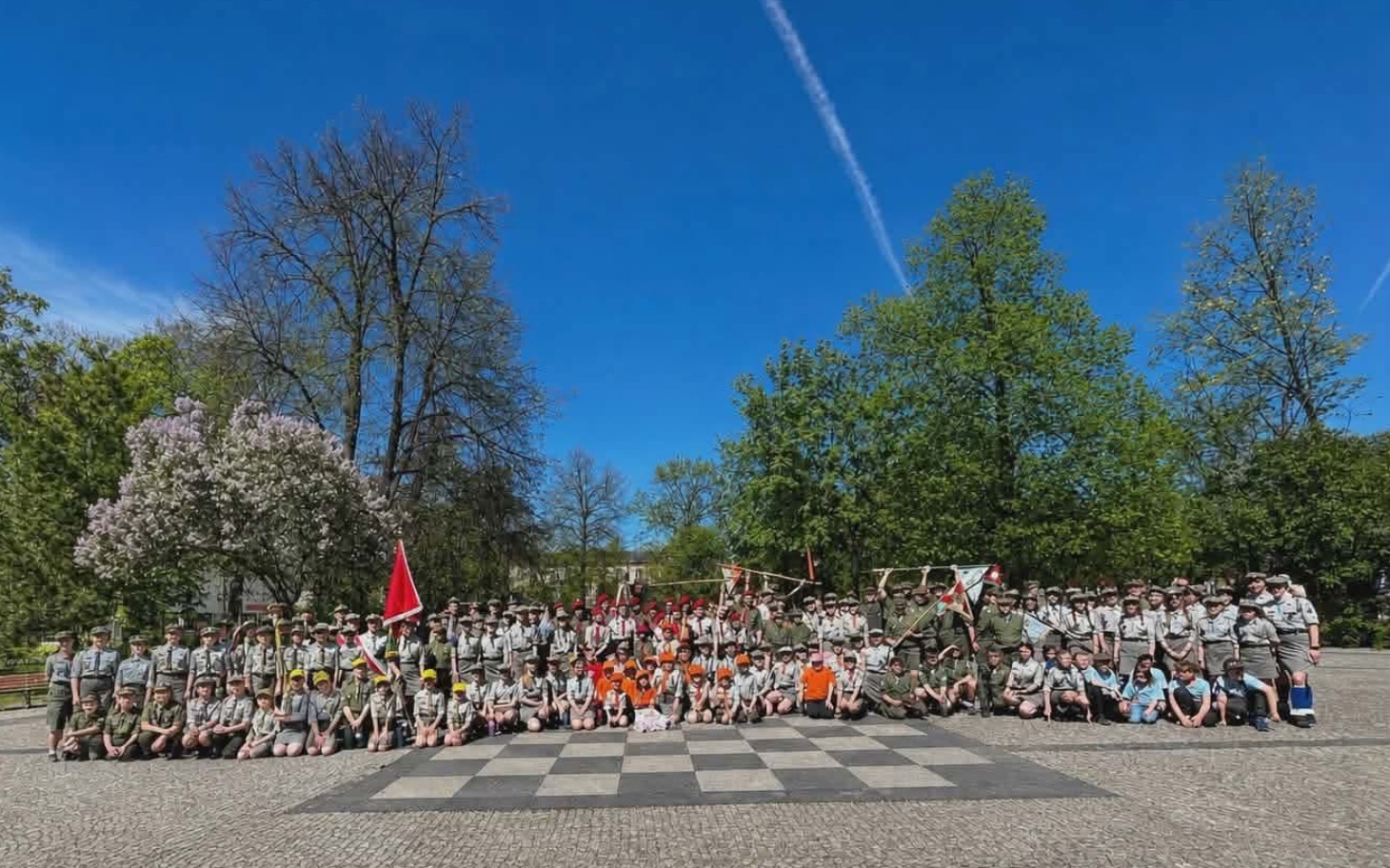
        Grupa młodych ludzi w mundurach, pozująca na placu.
    
