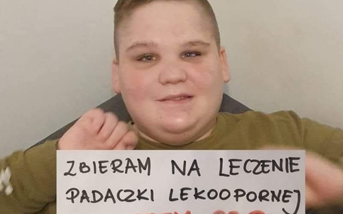 
        Chłopiec trzymający kartkę z prośbą o pomoc w leczeniu.
    