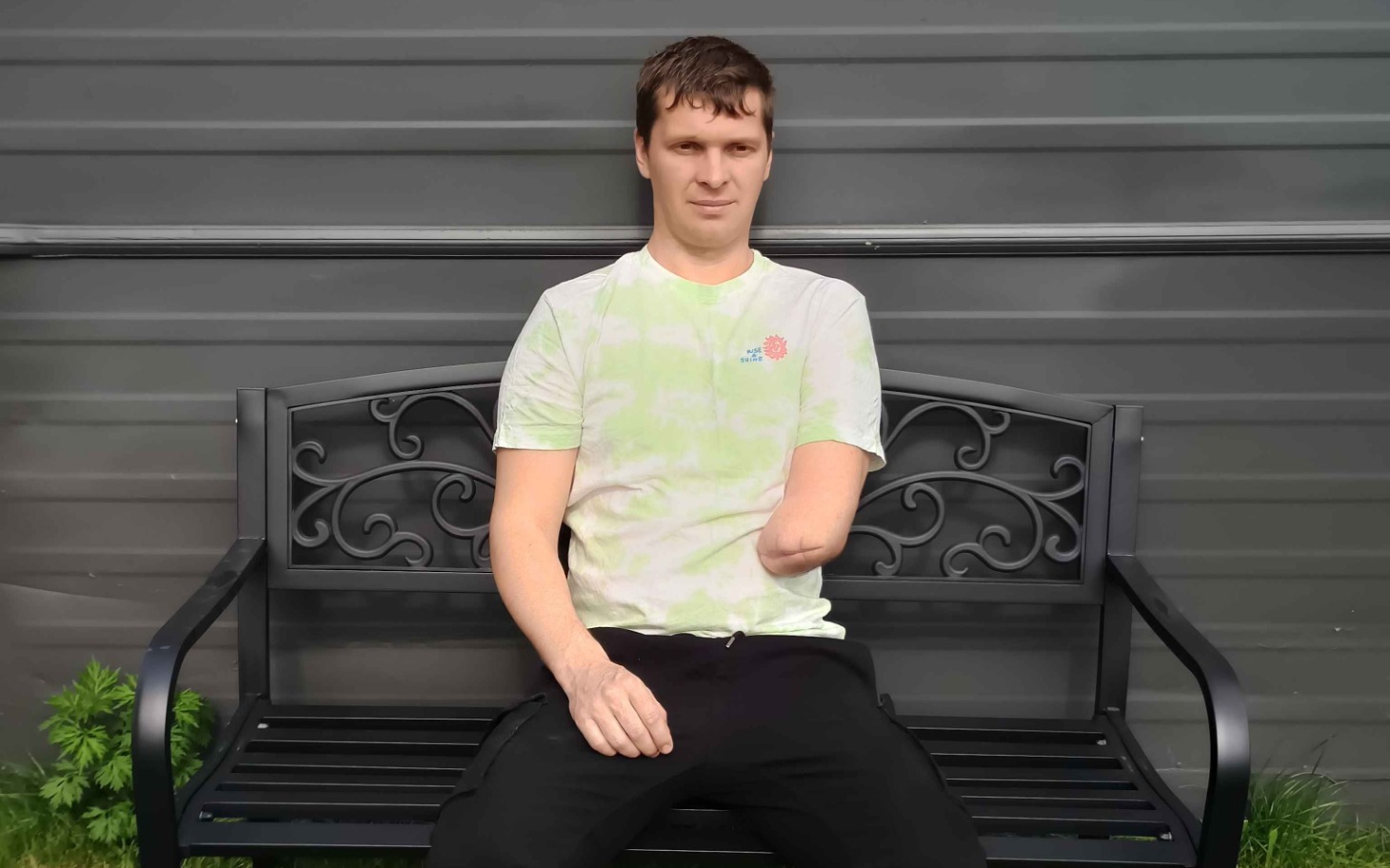 
        Mężczyzna na ławce, z jedną ręką, uśmiechnięty i pewny siebie.
    