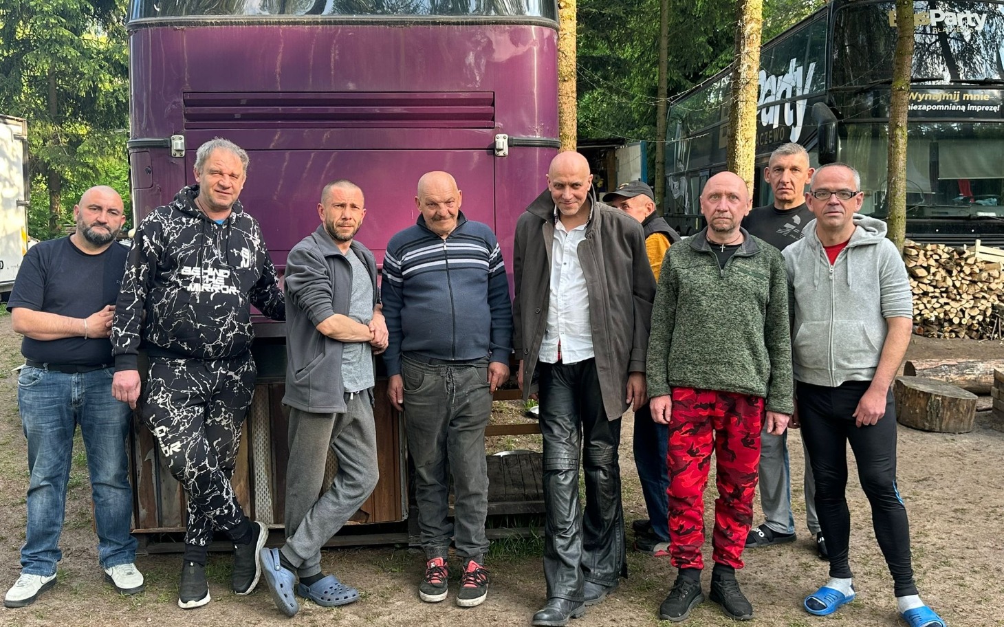 
        Grupa mężczyzn pozujących przed fioletowym autobusem.
    