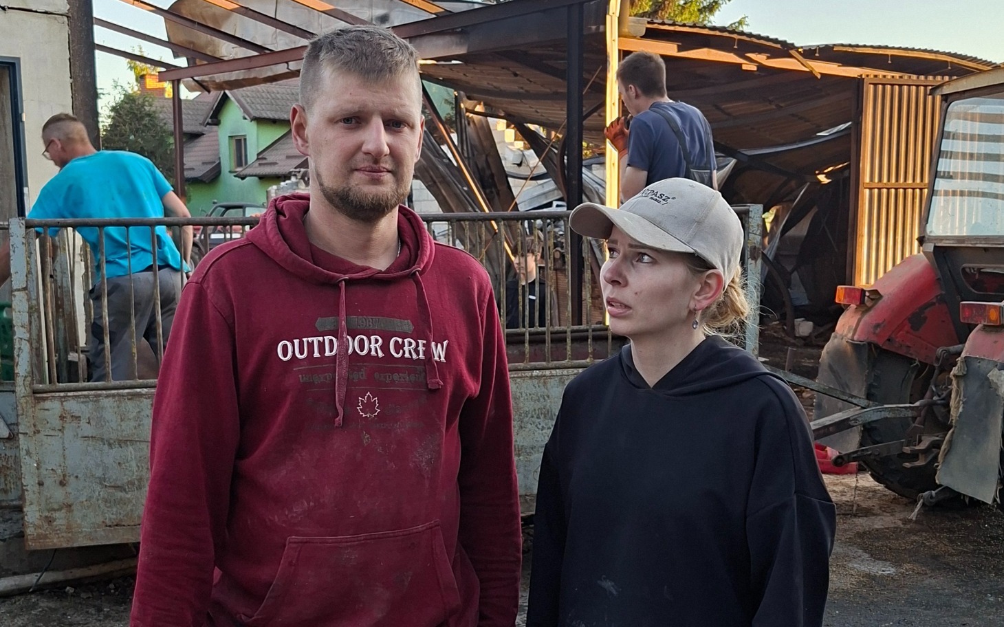 
        Para ludzi w trudnej sytuacji, rozmawiających na tle zniszczeń.
    