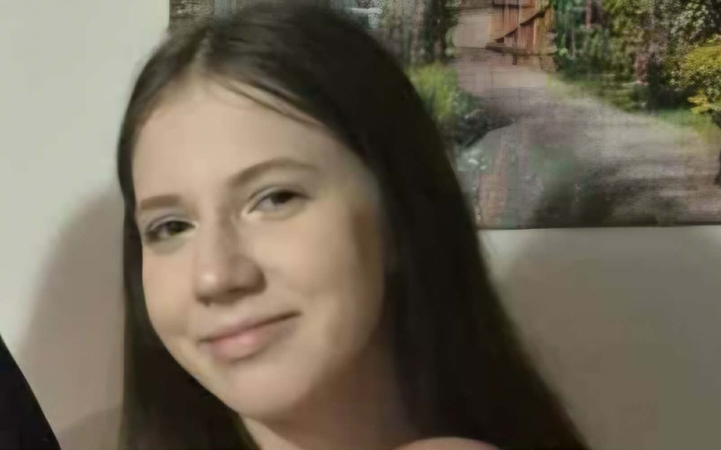 
        Młoda dziewczyna uśmiechająca się do kamery, w tle obrazek.
    
