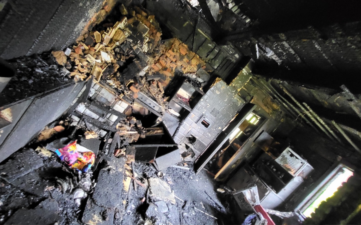 
        Zniszczone wnętrze domu po pożarze, pełne popiołu.
    