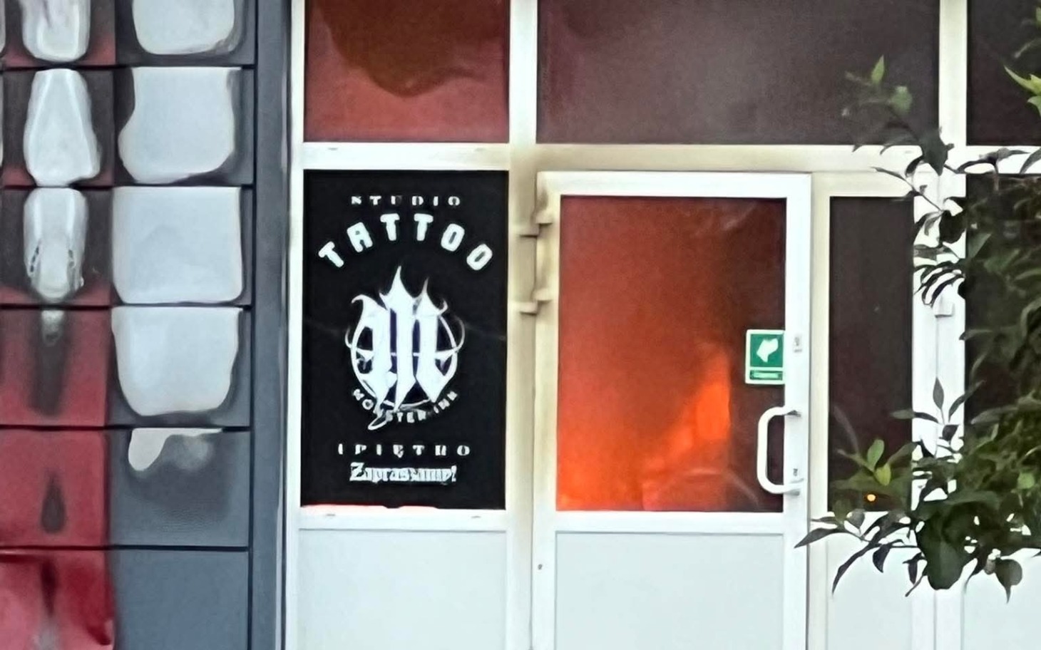 
        Wejście do studia tatuażu z widocznym logo.
    