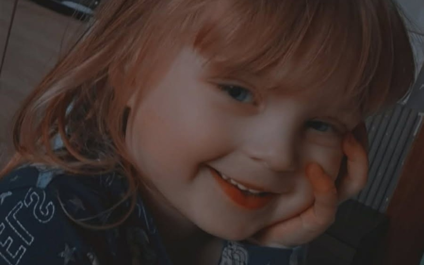 
        Dziewczynka z rudymi włosami uśmiecha się, opiera głowę na dłoni.
    