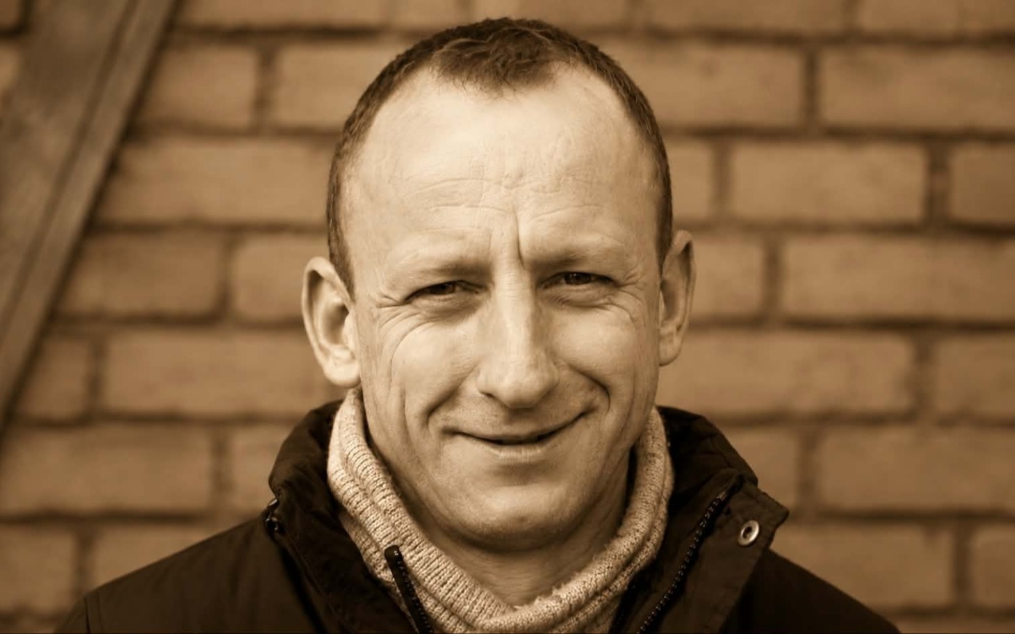 
        Uśmiechnięty mężczyzna na tle schodów (portret, ujęcie monochromatyczne).
    