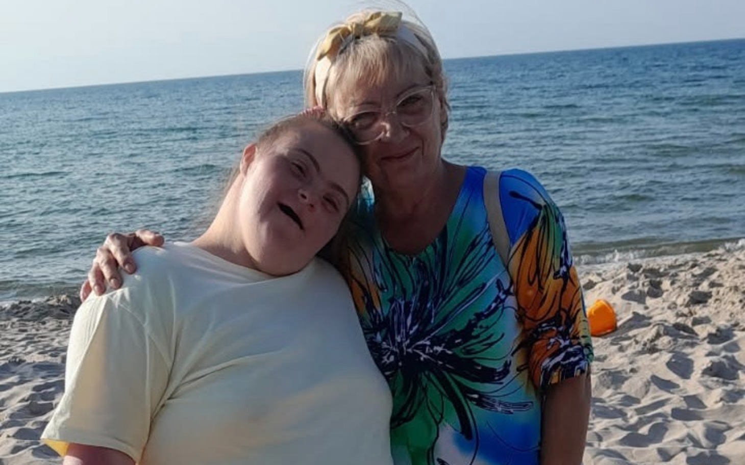 
        Dwie osoby na plaży przytulają się, uśmiech i lato nad morzem.
    