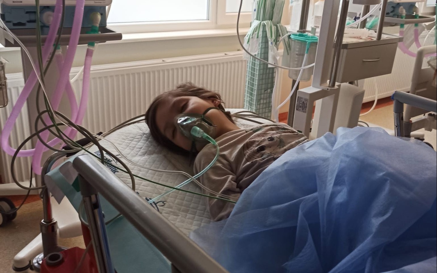 
        Pacjentka w szpitalnym łóżku z maseczką i monitorami wokół.
    