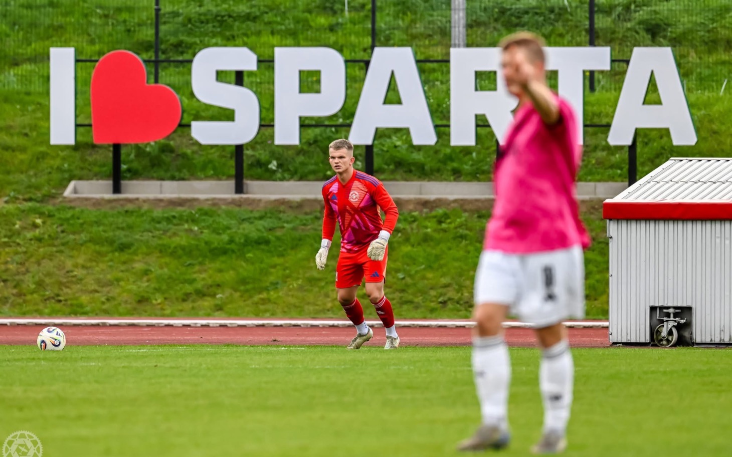 
        Gościu w czerwonej koszulce na boisku przed banną SPARTA
    