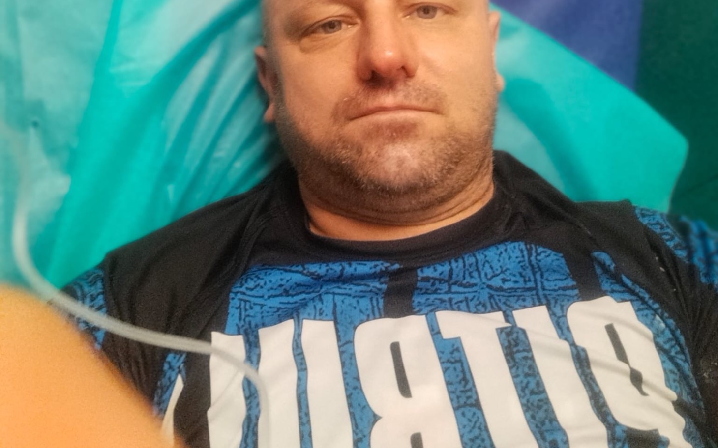 
        Mężczyzna leżący na stole w medycznym środowisku, opiera głowę.
    