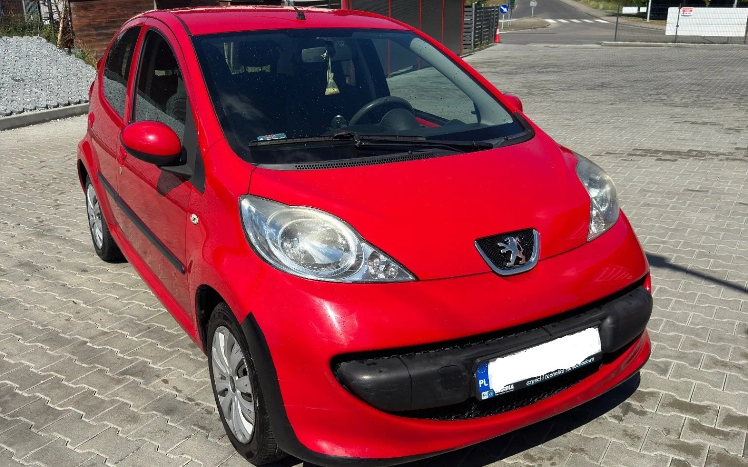 
        Uśmiechnięta osoba w białej koszulce na czerwonej elektrycznej maszcie samochodowej.
    