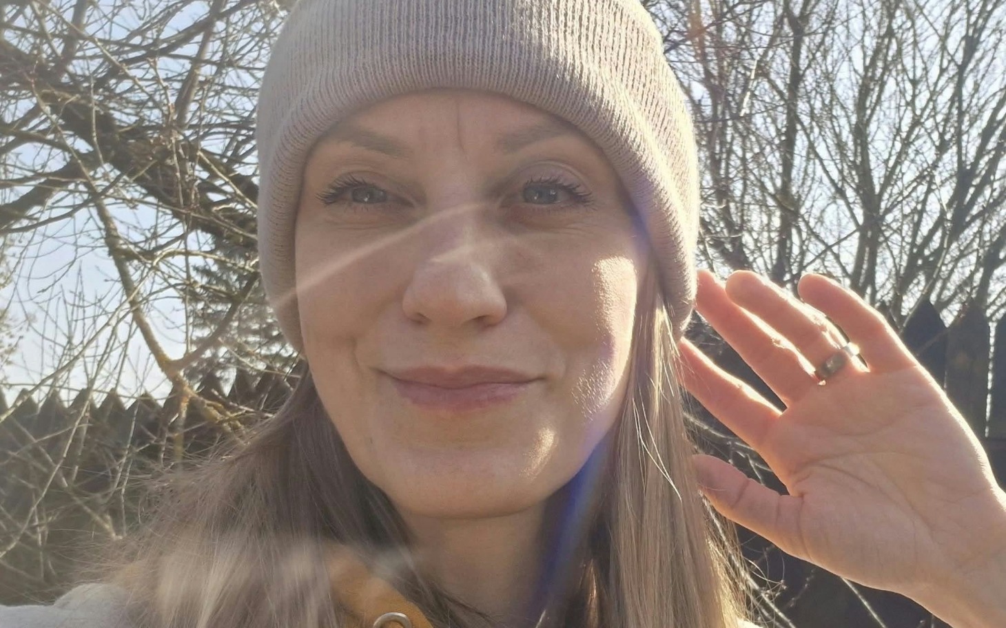 
        Uśmiechnięta kobieta na tle ogrodu w jesiennej pogodzie, macha dłonią do kamery.
    