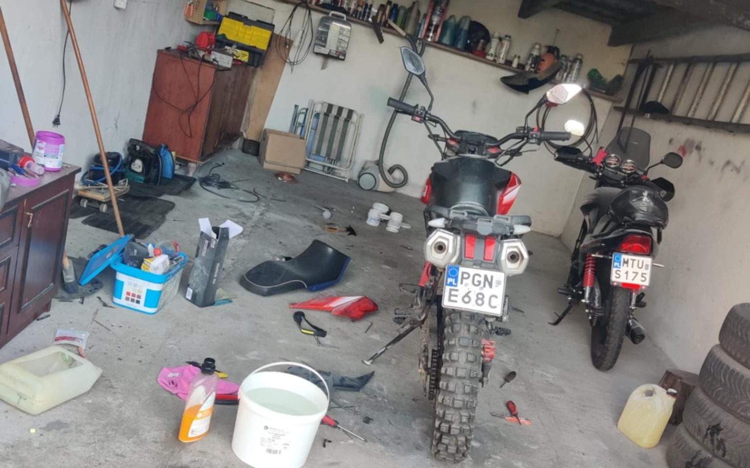 
        Zabałaganiona garaż, dwa motocykle i narzędzia rozrzucone.
    