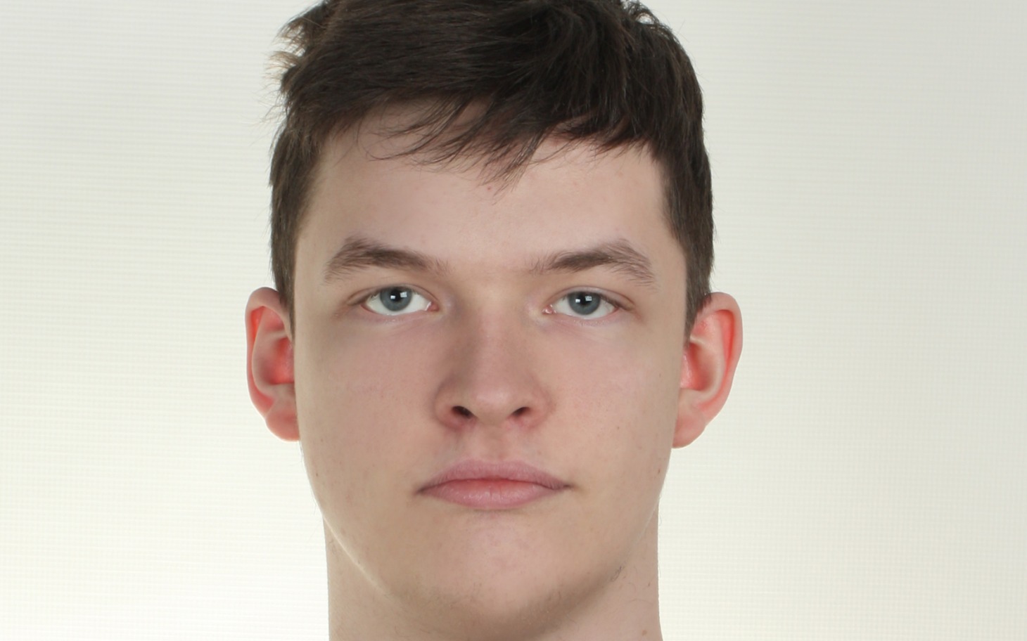 
        Młody mężczyzna z neutralnym wyrazem twarzy na jasnym tle.
    