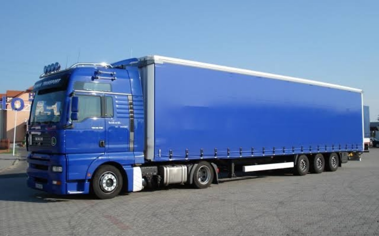 
        Niebieska ciężarówka zaparkowana na placu.
    