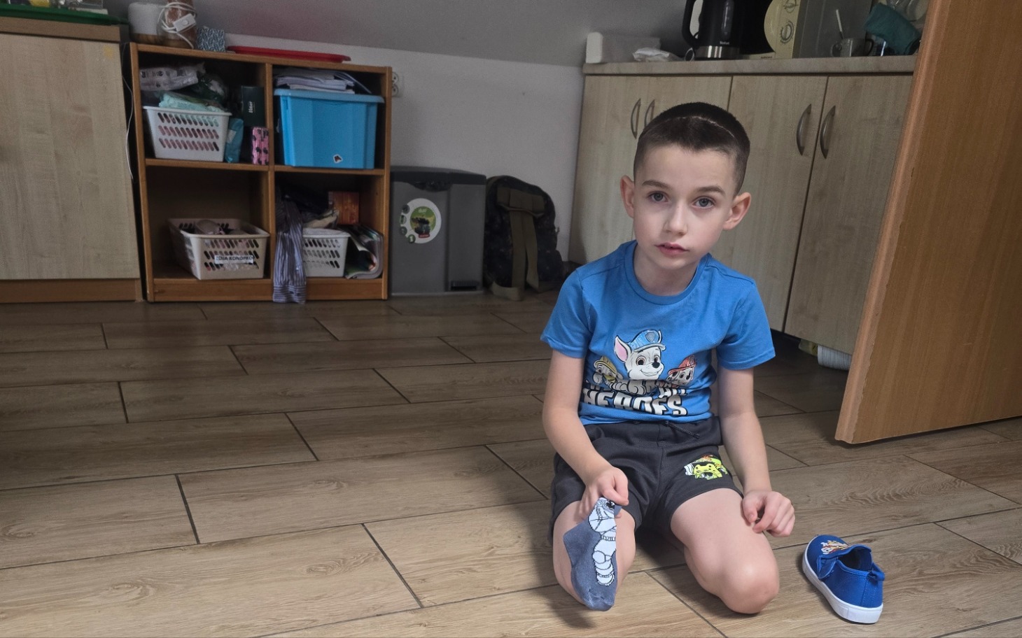 
        Chłopiec siedzący na podłodze, zakładający buty.
    