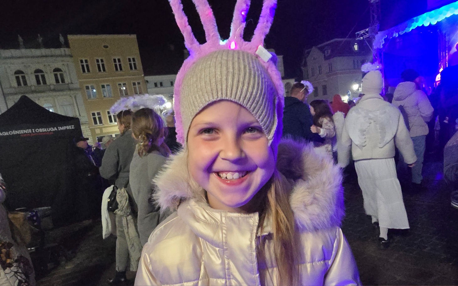 
        Uśmiechnięta dziewczynka w czapce z uszami na festiwalu.
    