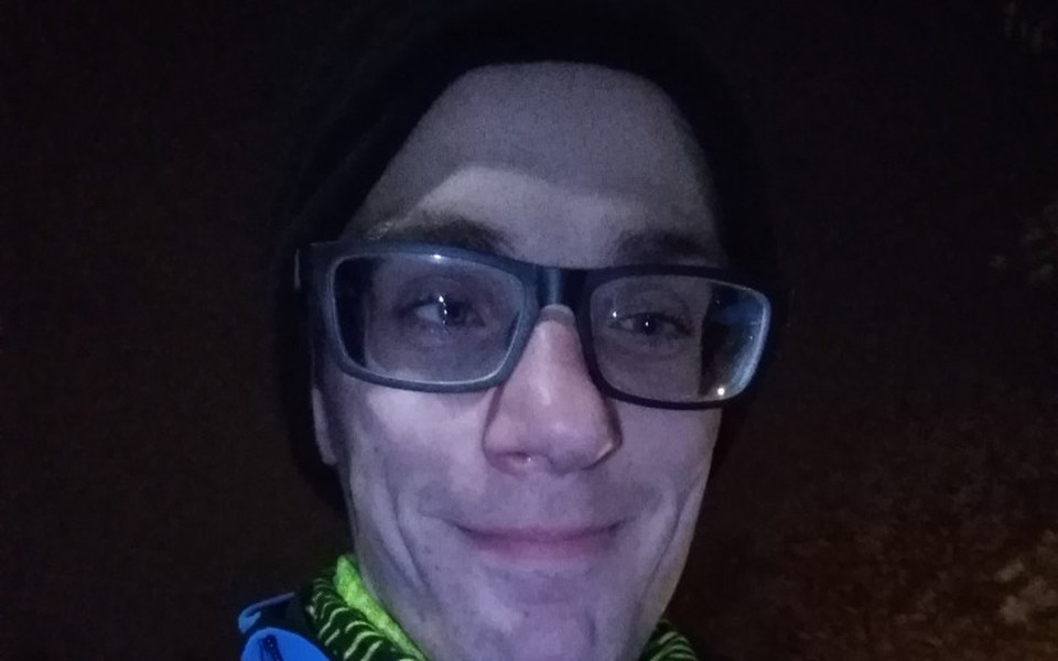 
        Mężczyzna w okularach, uśmiechający się w ciemnym otoczeniu.
    