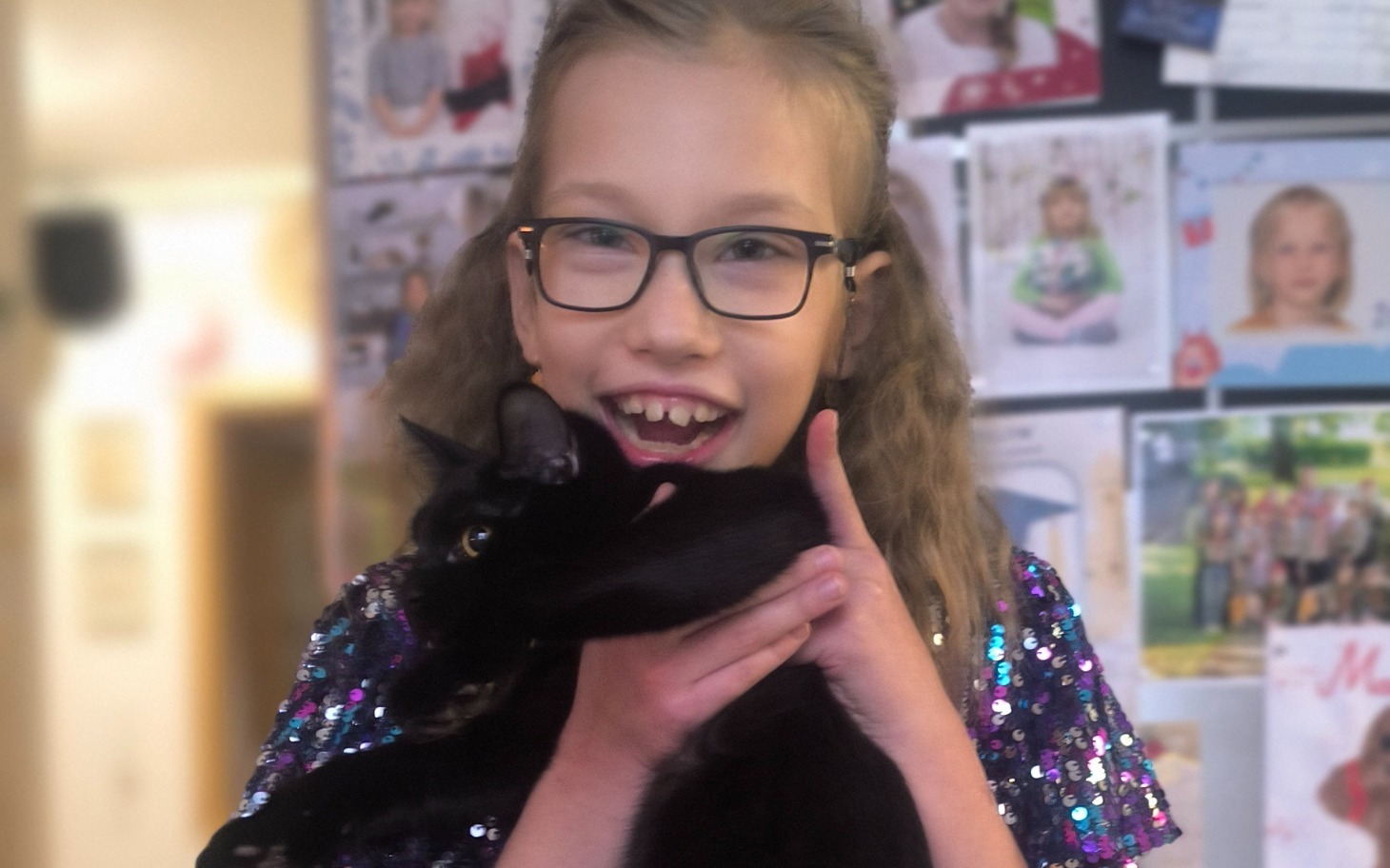 
        Dziewczynka z okularami trzymająca czarnego kota.
    