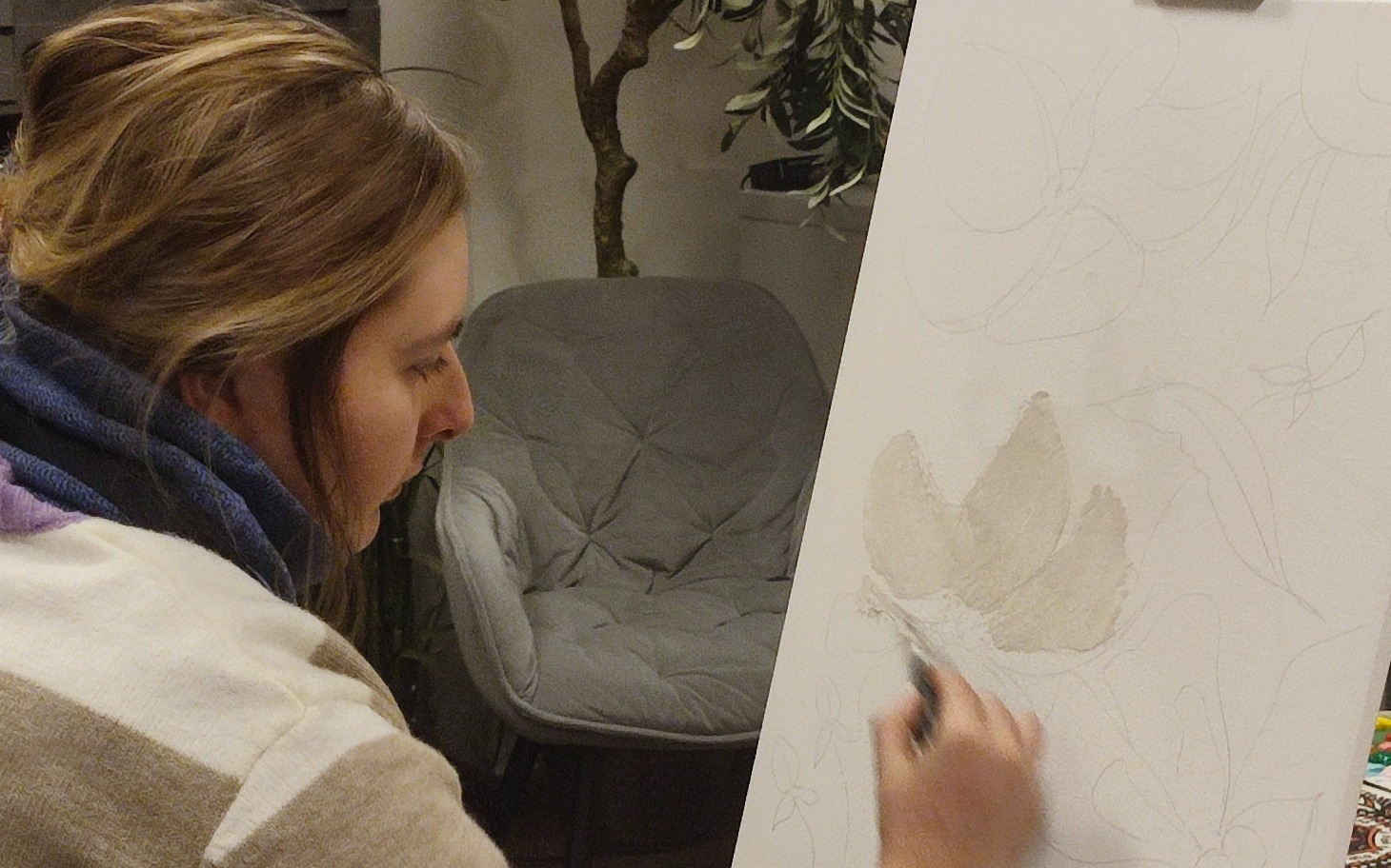 
        Kobieta malująca kwiaty na płótnie, skupiona na pracy.
    